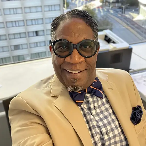 Smiling stylish Black man with yellow jacket, striped bow tie, checkered shirt and bold black tinted glasses