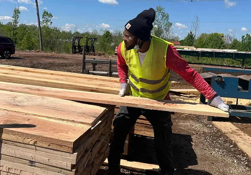 Man stacking boards of quality usable wood in a loading yard